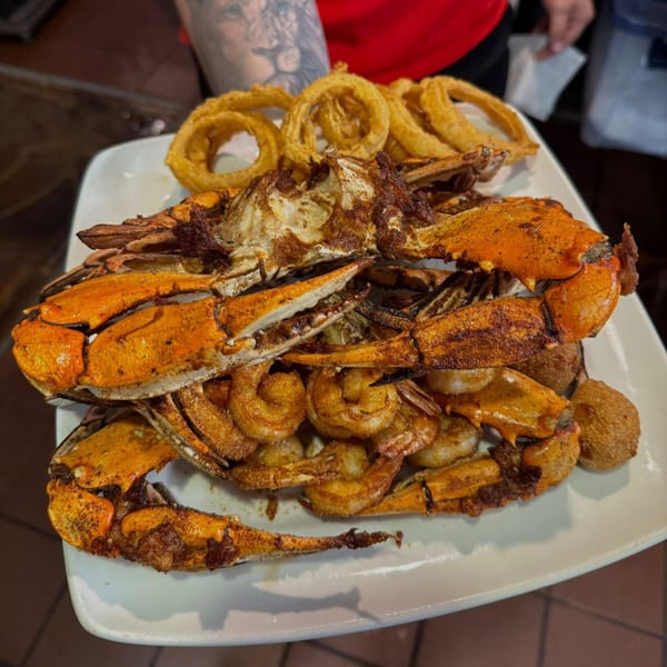 A platter of fried crab, shrimp, hush puppies, and onion rings held by a person.